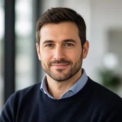 Professional portrait of a fictional adult author in smart casual attire, set against a softly blurred office background.